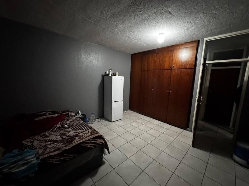 A bedroom featuring tiled flooring and a large built-in wooden wardrobe, requiring cosmetic updates to improve the overall aesthetic and lighting.