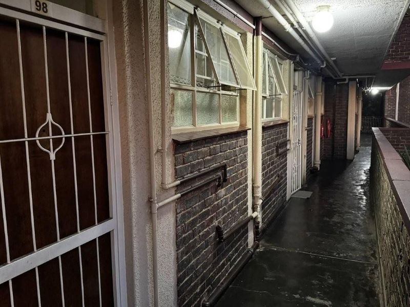 Exterior apartment hallway featuring exposed brickwork, security gates, and functional awning windows in a communal walkway area.