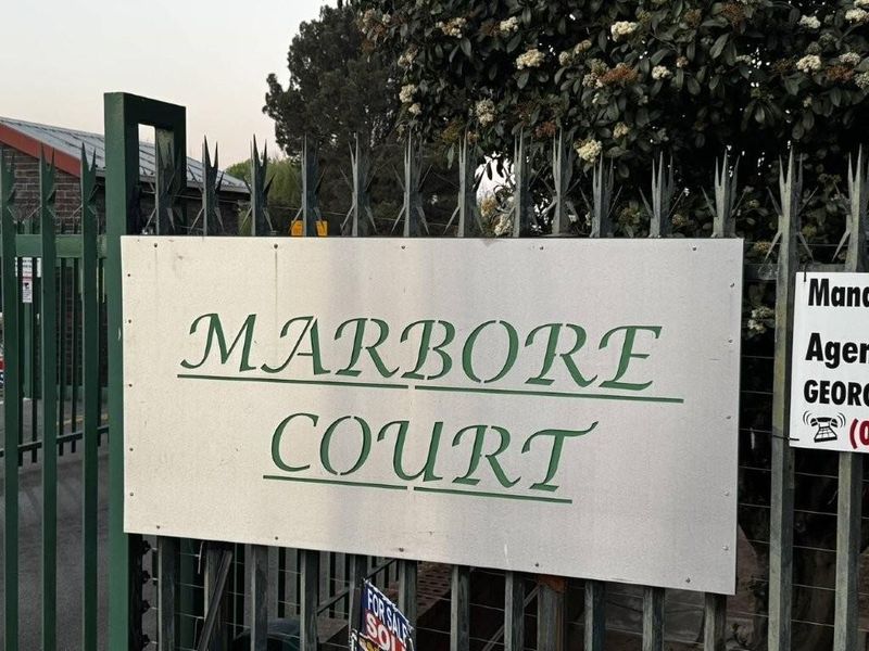 Entrance view of Marbore Court featuring metal security fencing and property signage.