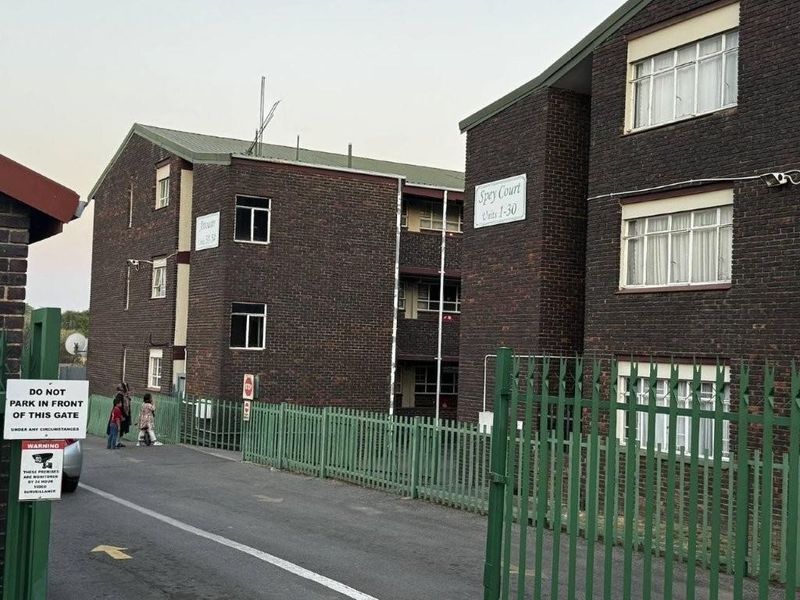 Exterior view of Spey Court apartment complex featuring brick facade, secure gated entrance, and paved driveway access.