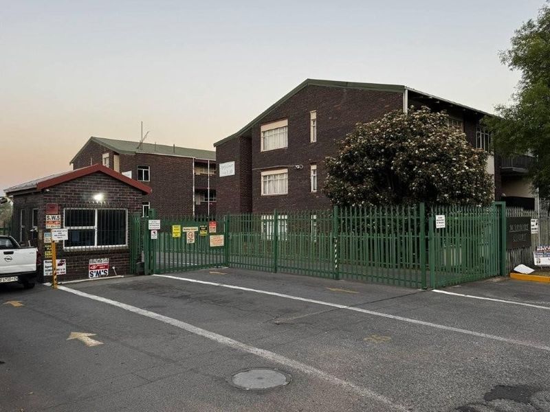 Exterior view of an apartment complex featuring a brick facade, secure gated entrance, and a dedicated guard house.