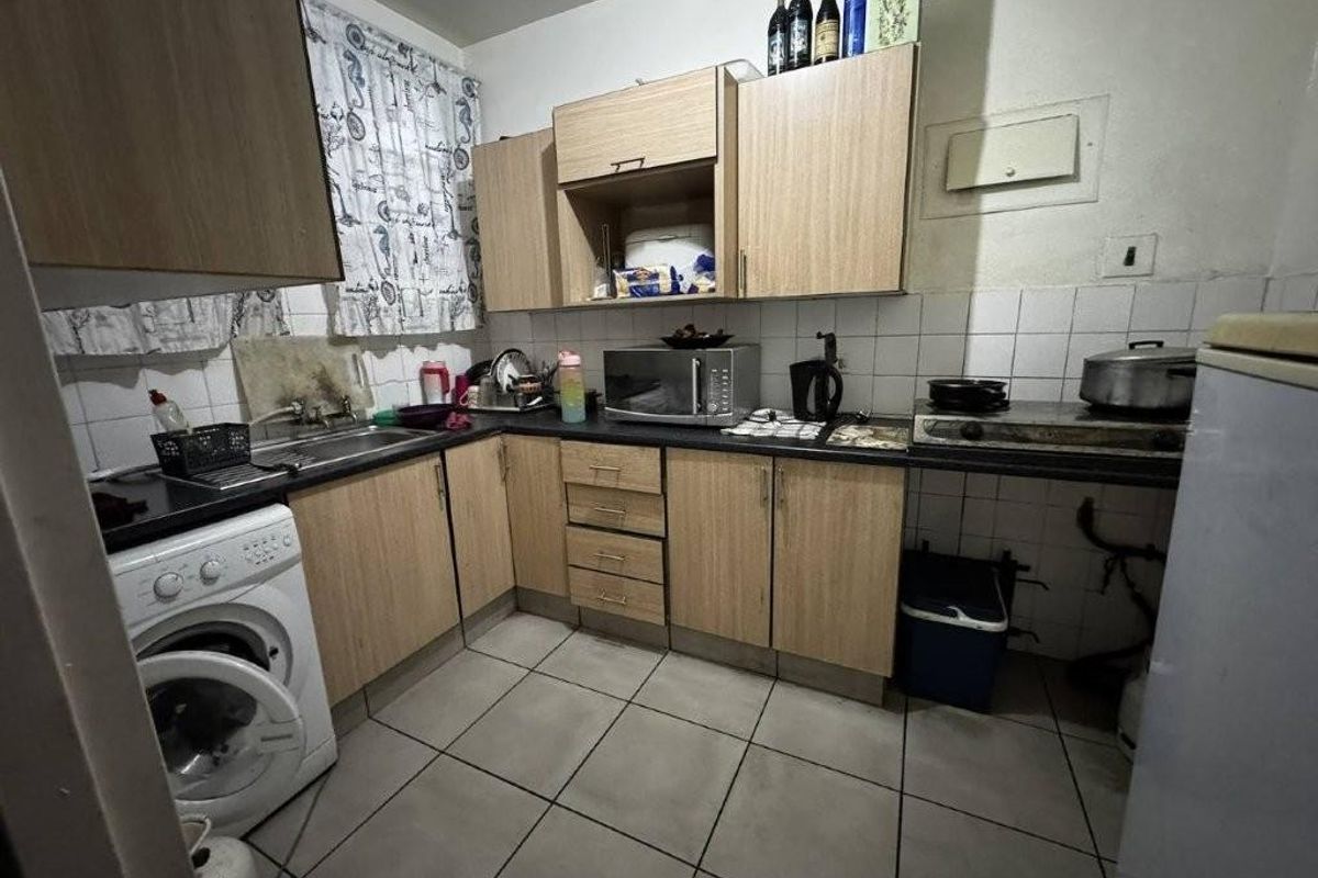 A compact kitchen featuring laminate cabinetry, tiled flooring, a built-in stove, and a dedicated space for a washing machine.
