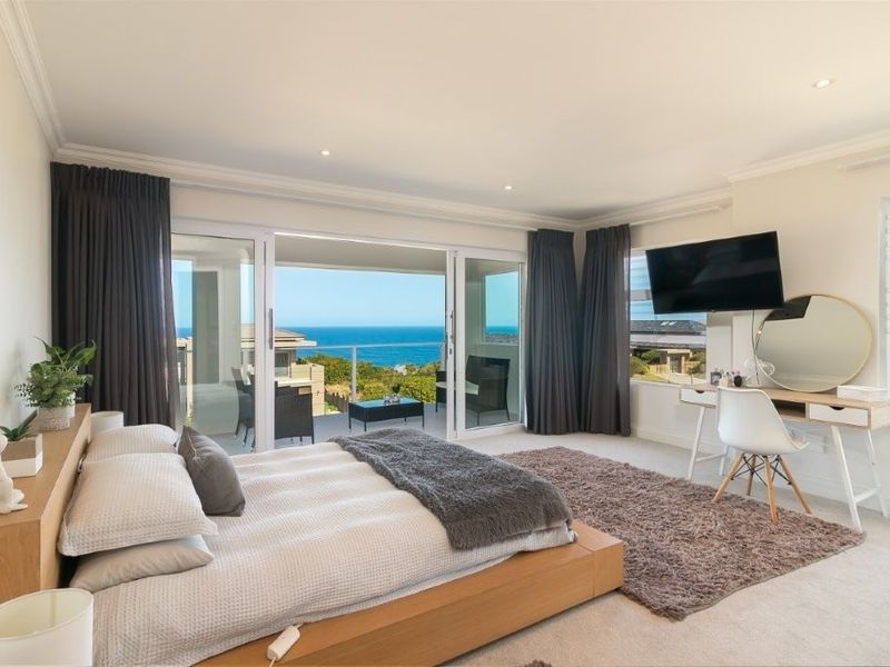 Spacious bedroom featuring neutral carpeting, crown molding, and large sliding glass doors opening to a balcony with expansive ocean views.