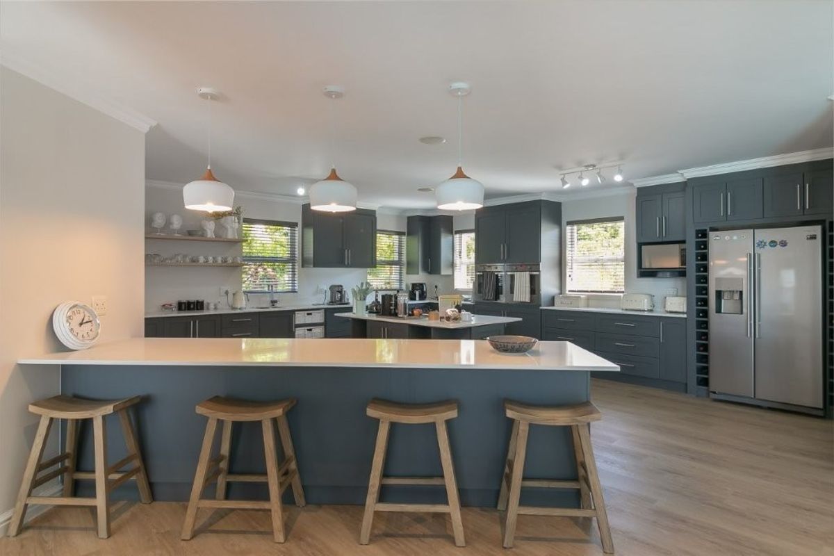Modern, spacious kitchen featuring a large central island with quartz countertops, dark cabinetry, double wall ovens, and integrated wine storage.