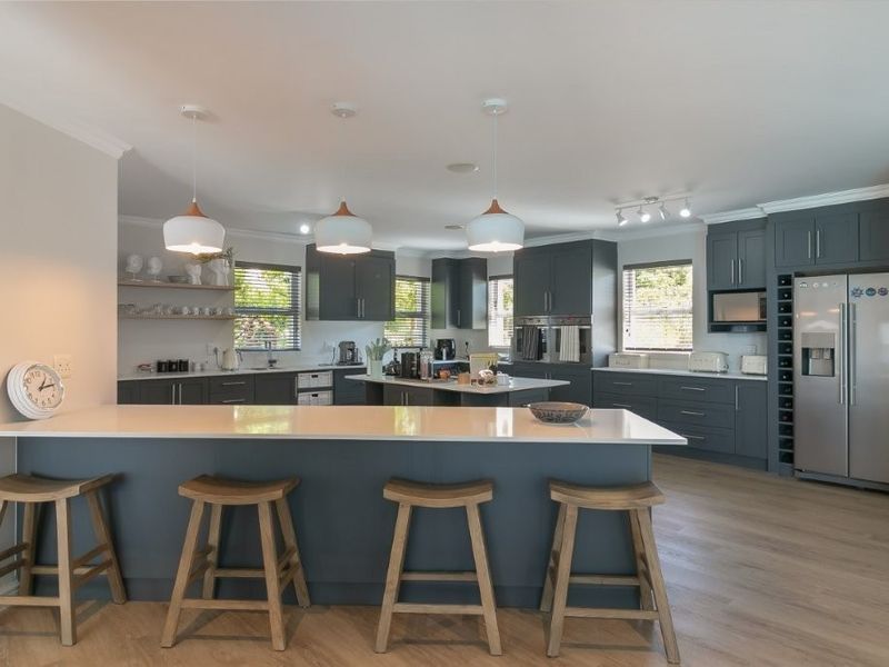 Modern, spacious kitchen featuring a large central island with quartz countertops, dark cabinetry, double wall ovens, and integrated wine storage.