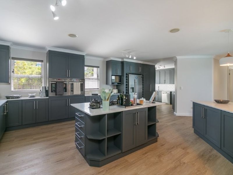 Spacious open-plan kitchen featuring dark grey cabinetry, a central island with storage, quartz countertops, and modern built-in appliances.
