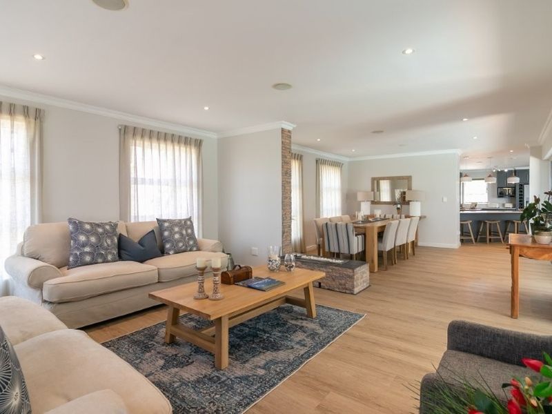 Spacious open-plan living and dining area featuring timber flooring, recessed lighting, and a stone feature pillar, seamlessly flowing into a modern kitchen.