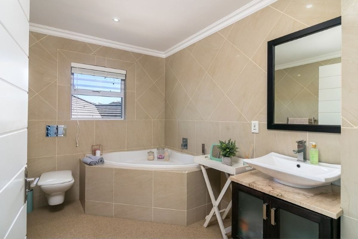 Modern bathroom featuring a corner bathtub, wall-mounted toilet, and a vanity with a vessel sink, finished with neutral wall tiles.