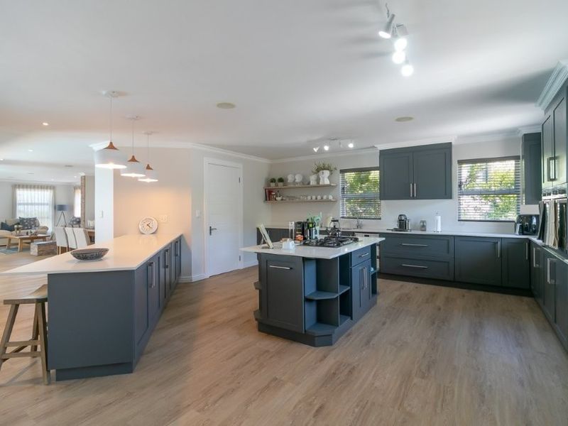 Spacious open-plan kitchen featuring modern dark cabinetry, stone countertops, a central island with a gas hob, and high-quality laminate flooring.