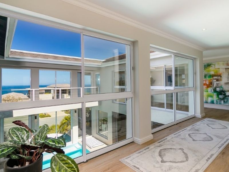 A bright, modern hallway featuring extensive floor-to-ceiling sliding glass windows that offer views of the exterior courtyard and ocean.