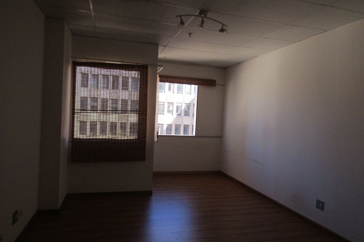 An empty bedroom featuring laminate flooring, a drop ceiling with track lighting, and bamboo blinds on the windows.