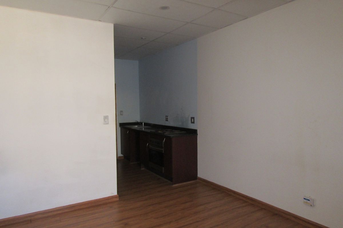 An empty kitchen area featuring dark cabinetry, a built-in oven, hob, and sink, set against a backdrop of plain walls and laminate flooring.