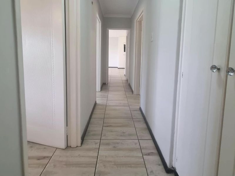 A clean, neutral hallway featuring light wood-look floor tiles, multiple internal doors, and built-in storage cupboards.