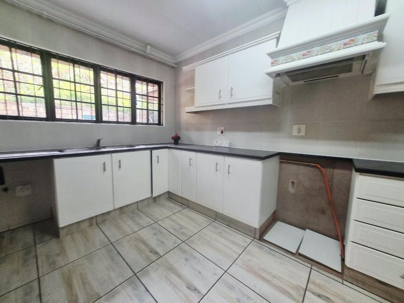 A functional kitchen space featuring white cabinetry, dark countertops, and tiled flooring, currently awaiting the installation of a stove or oven unit.