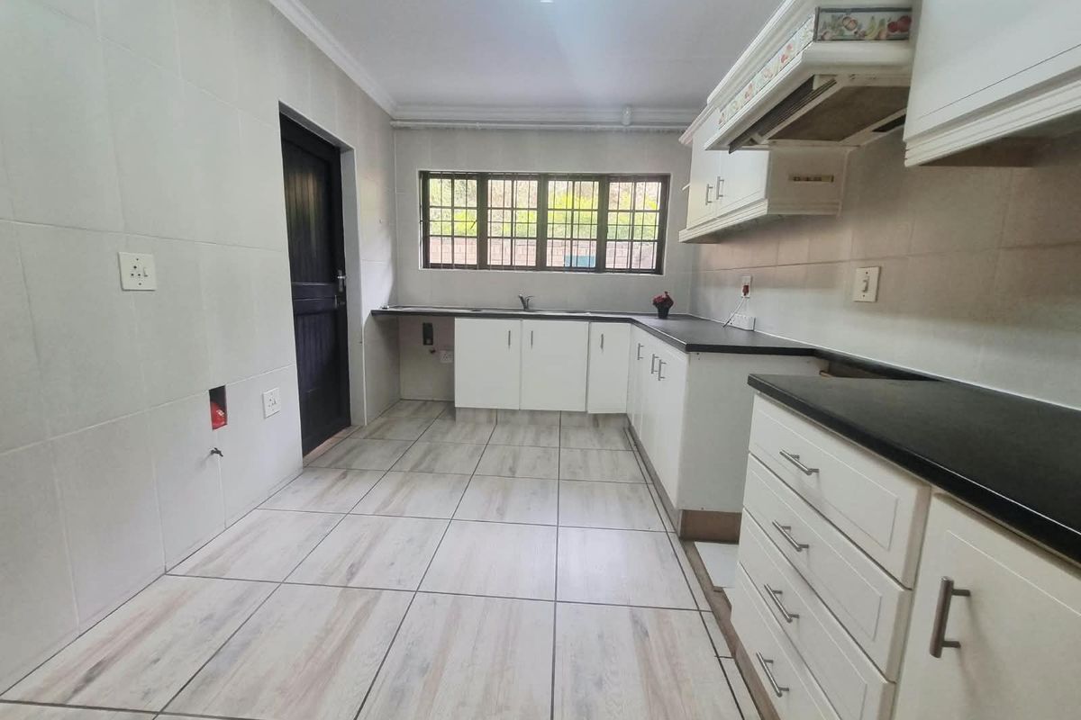 A clean, empty kitchen featuring white cabinetry, dark countertops, tiled flooring, and wall tiling, providing a functional blank canvas for customization.