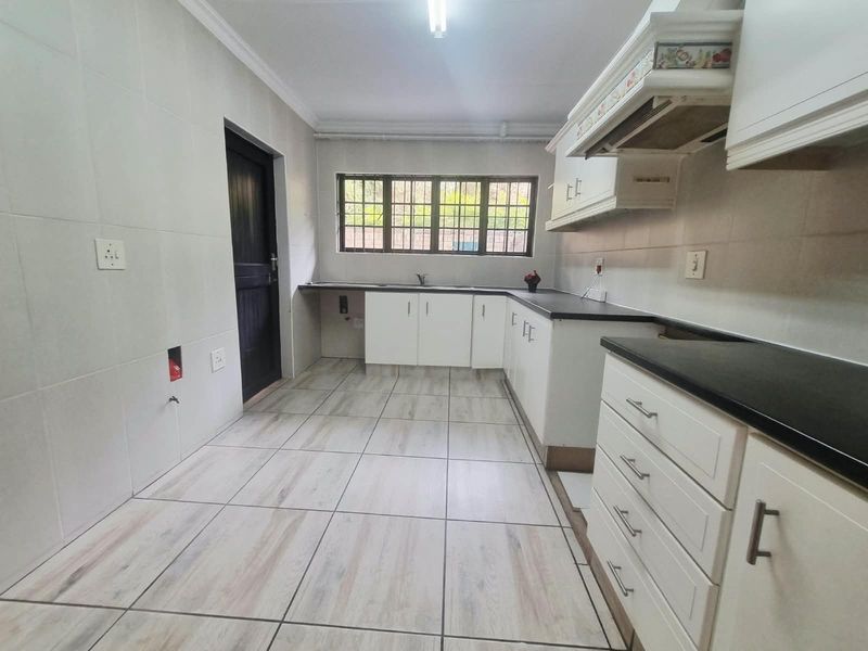A clean, empty kitchen featuring white cabinetry, dark countertops, tiled flooring, and wall tiling, providing a functional blank canvas for customization.
