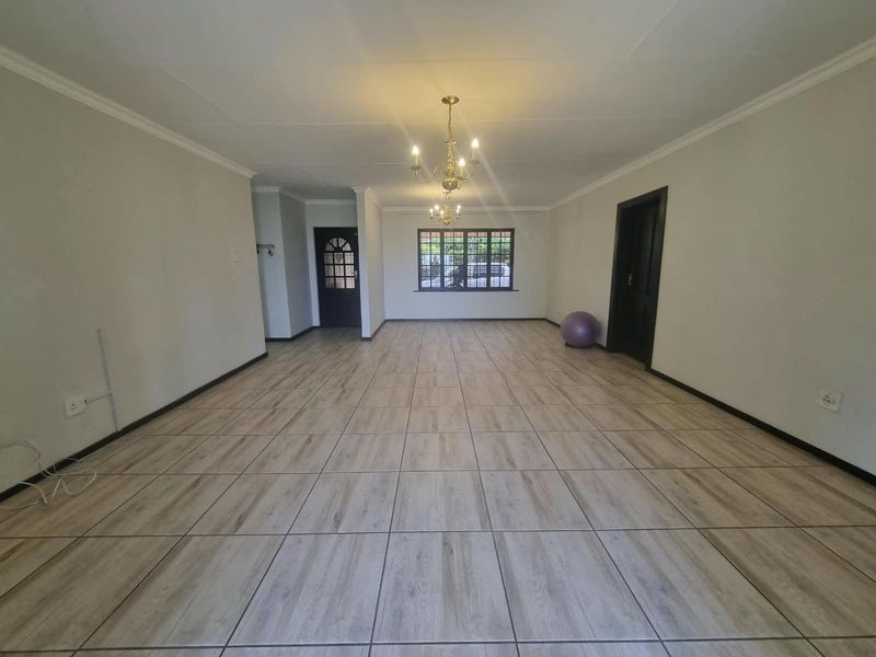 A spacious, empty living area featuring neutral tiled flooring, coved ceilings, and a classic chandelier, offering a versatile blank canvas for interior design.
