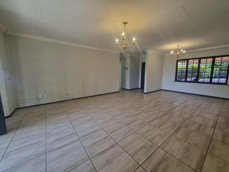 Spacious, open-plan living area featuring neutral tiled flooring, coved ceilings, and classic chandelier lighting, offering a bright and versatile space.