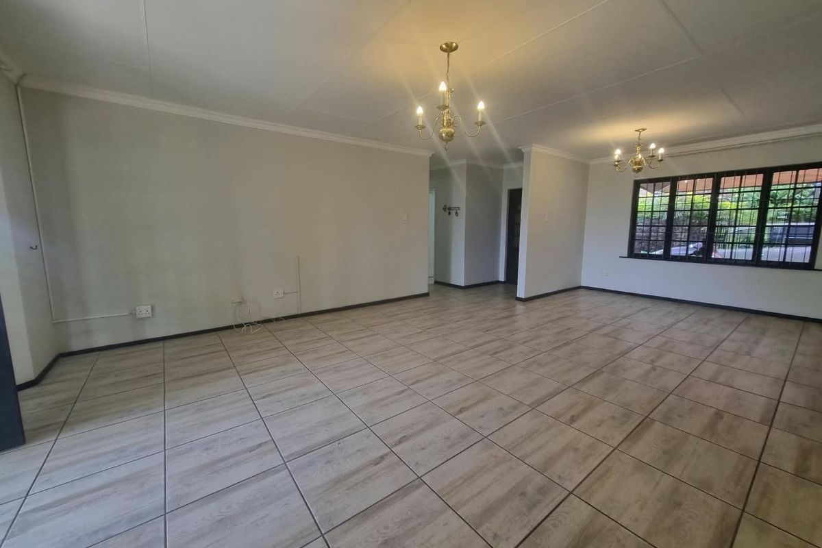 Spacious, open-plan living area featuring neutral tiled flooring, coved ceilings, and classic chandelier lighting, offering a bright and versatile space.