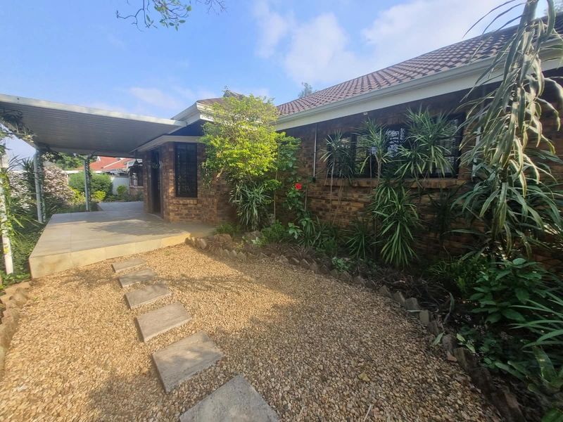 A well-maintained rear exterior view of a face brick townhouse featuring a covered patio, paved walkway, and established garden area.