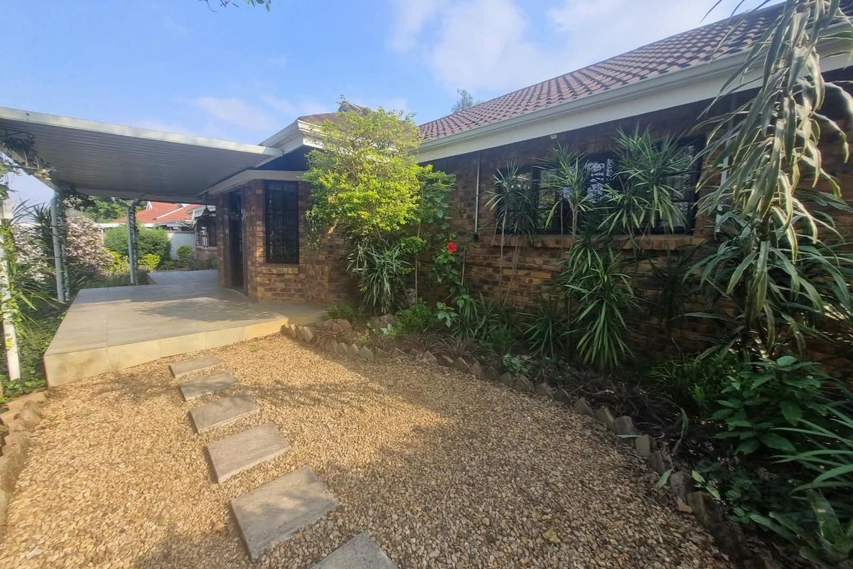 A well-maintained rear exterior view of a face brick townhouse featuring a covered patio, paved walkway, and established garden area.