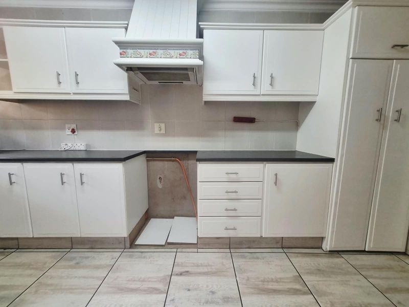 A kitchen featuring white cabinetry, tiled flooring, and a dedicated space for an appliance with exposed plumbing connections.