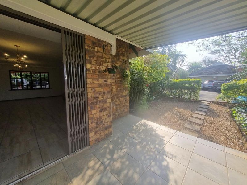 A covered patio area featuring tiled flooring, brick wall detailing, and a security gate leading into the interior living space.