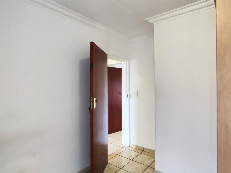 A clean, empty hallway featuring neutral white walls, crown molding, and tiled flooring, providing a simple transition between rooms.