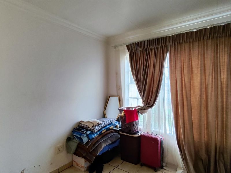 A bedroom featuring tiled flooring and a window with curtain rails, showing signs of wear on the walls.