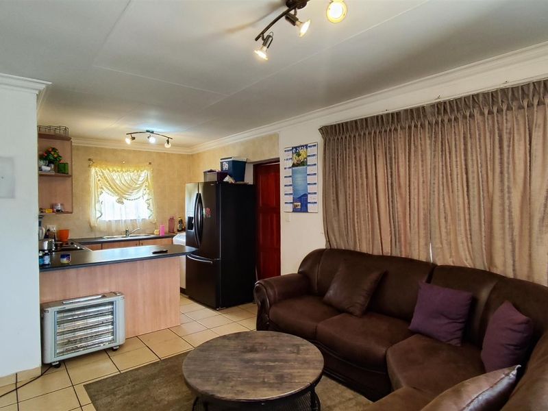 Open-plan living area featuring a functional kitchen with island, tiled flooring, and integrated track lighting, creating a combined space for cooking and relaxation.