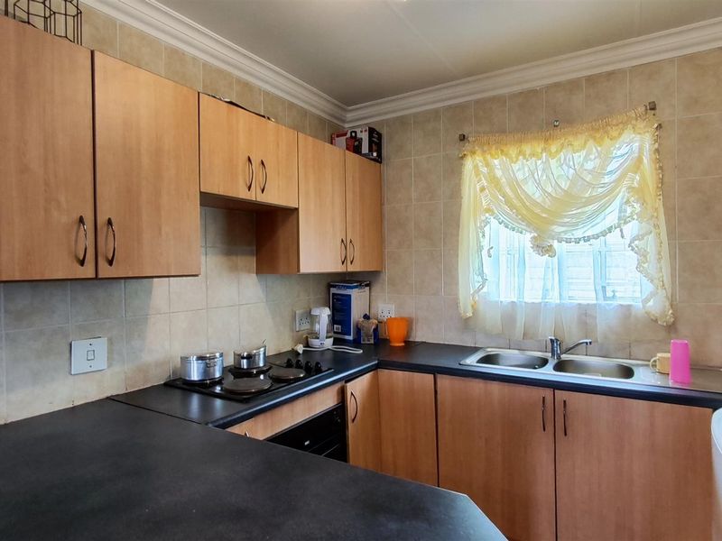 A functional kitchen featuring laminate cabinetry, dark countertops, a double bowl sink, and built-in cooking appliances with tiled wall finishes.