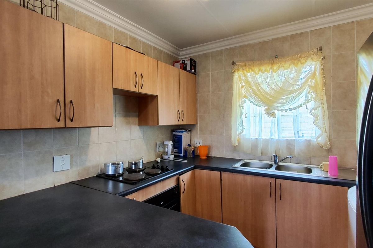 A functional kitchen featuring laminate cabinetry, dark countertops, a double bowl sink, and built-in cooking appliances with tiled wall finishes.