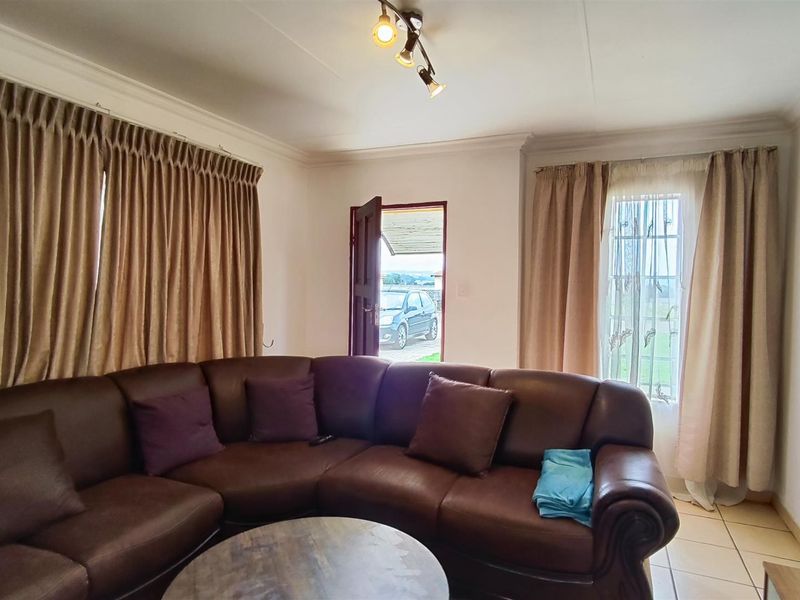 A living room featuring tiled flooring, ceiling coving, and track lighting, with direct access to the exterior via a security gate.