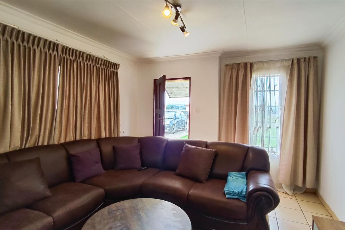 A living room featuring tiled flooring, ceiling coving, and track lighting, with direct access to the exterior via a security gate.