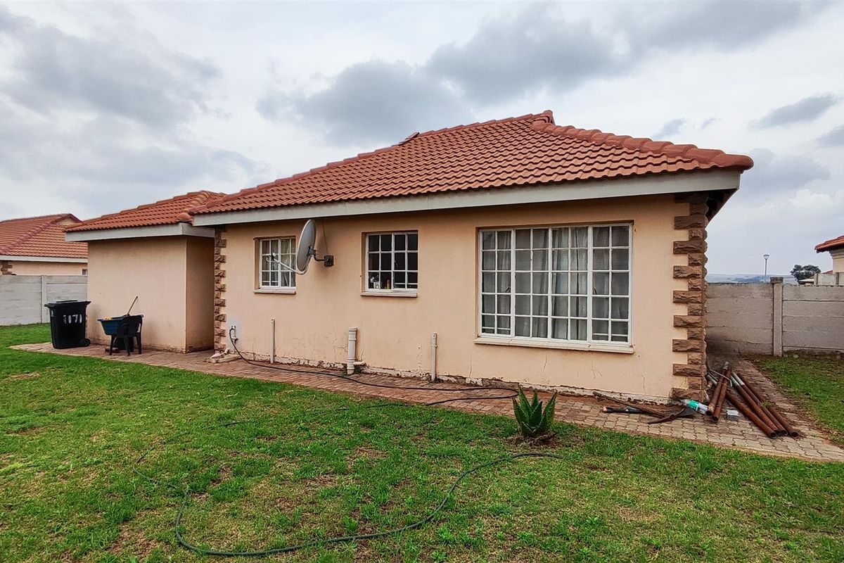Rear view of a single-story house featuring a terracotta tiled roof, brick corner detailing, and a paved walkway leading along the exterior wall.