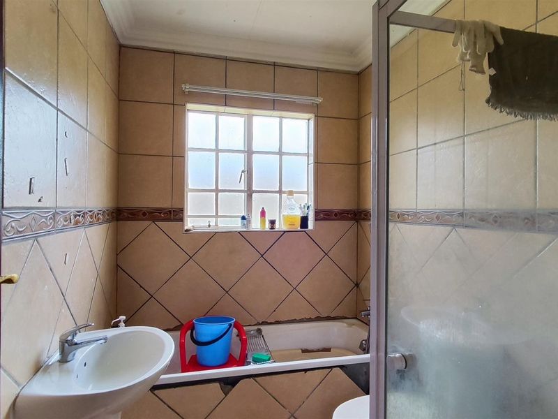 A dated bathroom featuring a pedestal basin, built-in bathtub, and shower enclosure with tiled walls requiring maintenance and cosmetic updates.