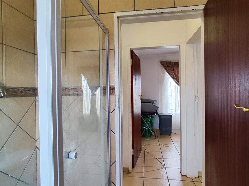 A functional bathroom featuring a glass shower enclosure with ceramic wall and floor tiling, leading into an adjacent room.