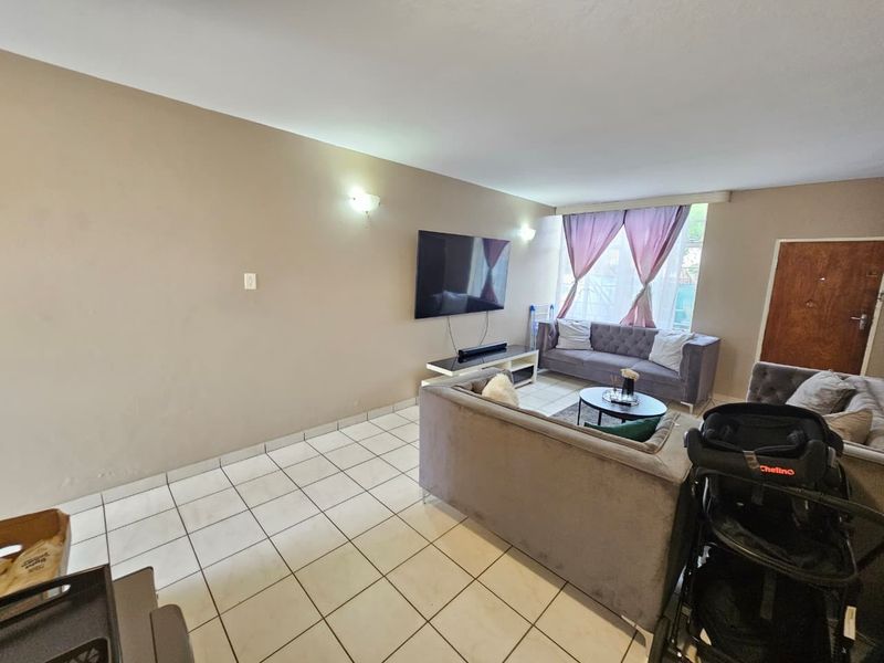 A spacious living room featuring neutral wall tones, tiled flooring, and natural light from a large window.