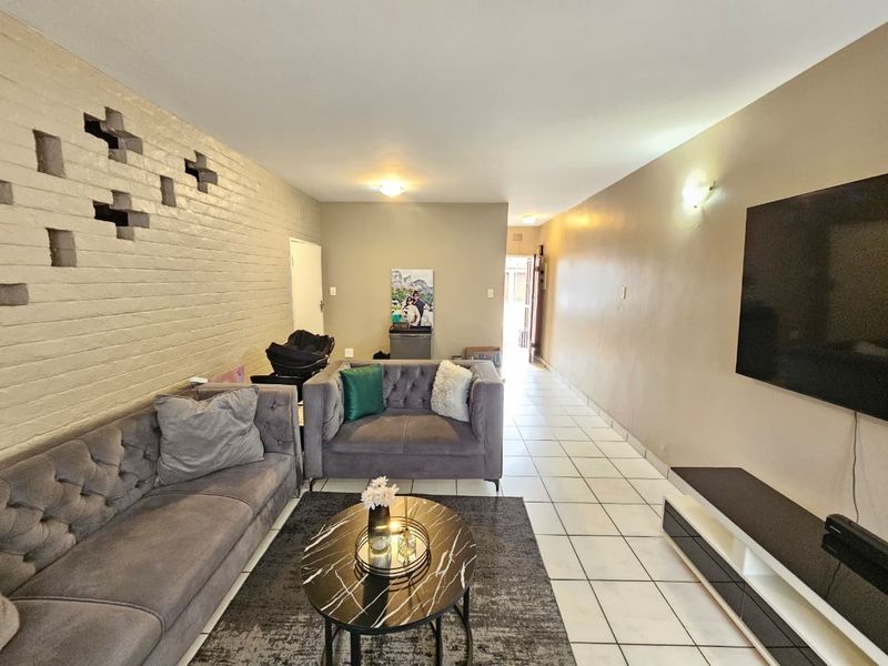 Spacious living room featuring a unique breeze block accent wall, neutral tiled flooring, and a wall-mounted television setup.