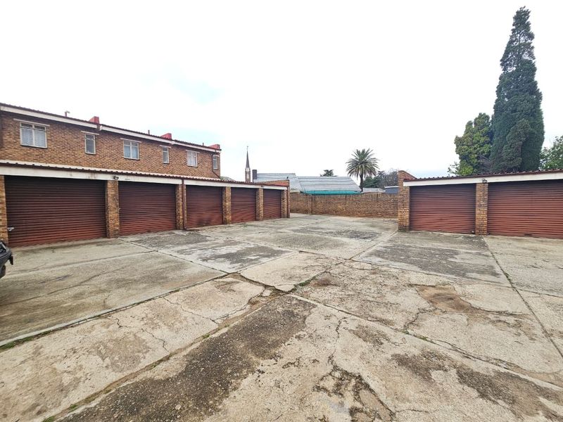 A communal parking area featuring multiple roller shutter garage doors and a weathered concrete driveway surface.