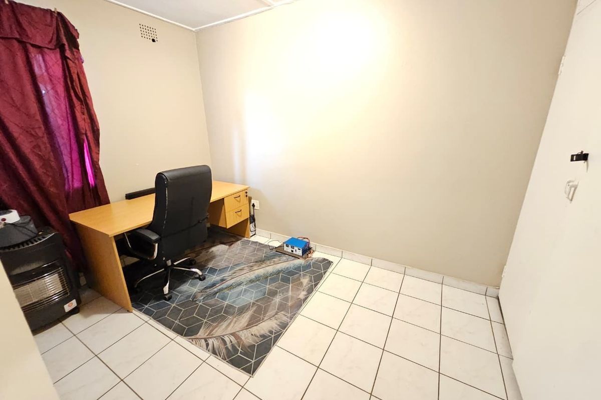 A functional bedroom space featuring neutral wall finishes and durable tiled flooring, suitable for use as a home office or guest room.