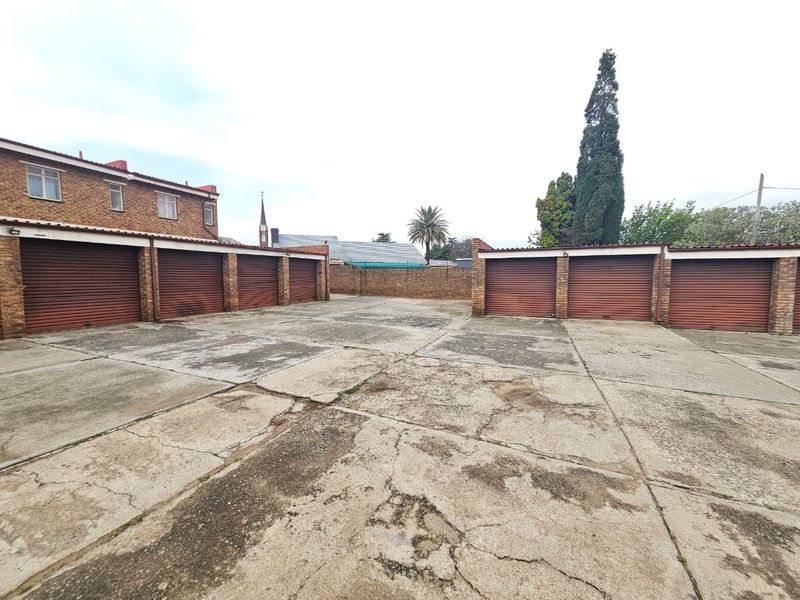 A communal parking area featuring multiple individual roller shutter garage doors and a weathered concrete driveway surface.