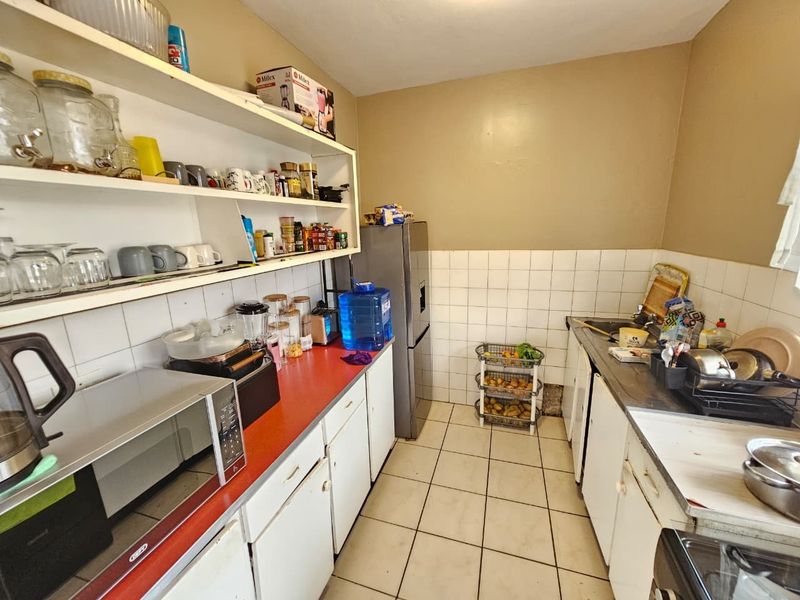 A functional kitchen featuring tiled flooring, a double sink, and open shelving, offering a practical layout with potential for modern updates.