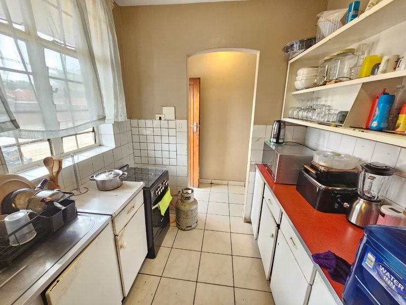 A functional kitchen featuring tiled flooring, built-in cabinetry, a stainless steel sink, and a freestanding stove, offering potential for modernization and cosmetic updates.