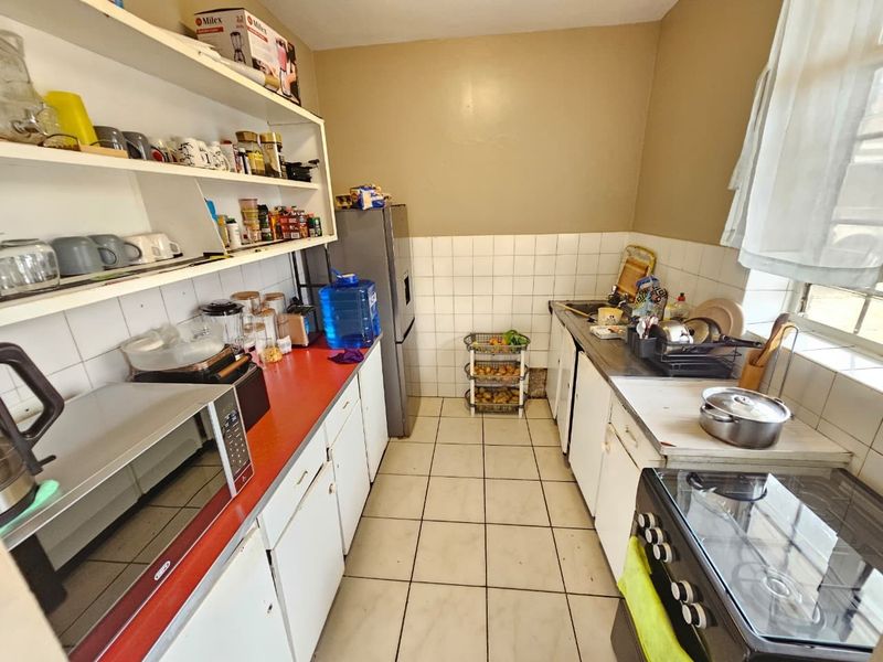A functional scullery area featuring tiled flooring, built-in cabinetry, open shelving, and a stainless steel sink with a tiled splashback.