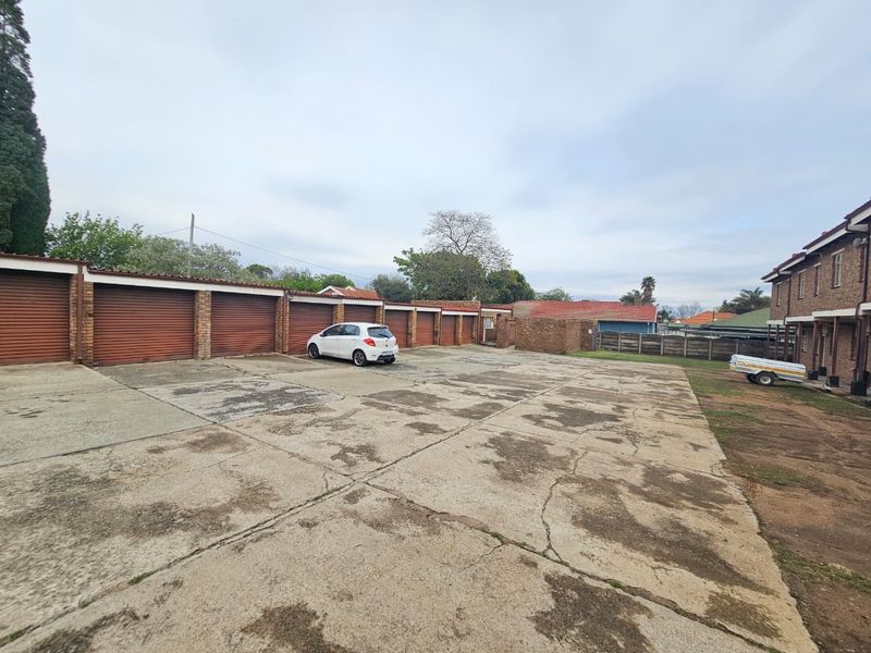 A row of multiple garage units with roller shutter doors and a large, weathered concrete driveway area.