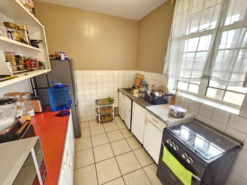 A functional kitchen featuring tiled flooring, a tiled backsplash, built-in cabinetry, and a freestanding stove, offering potential for modernization and cosmetic updates.