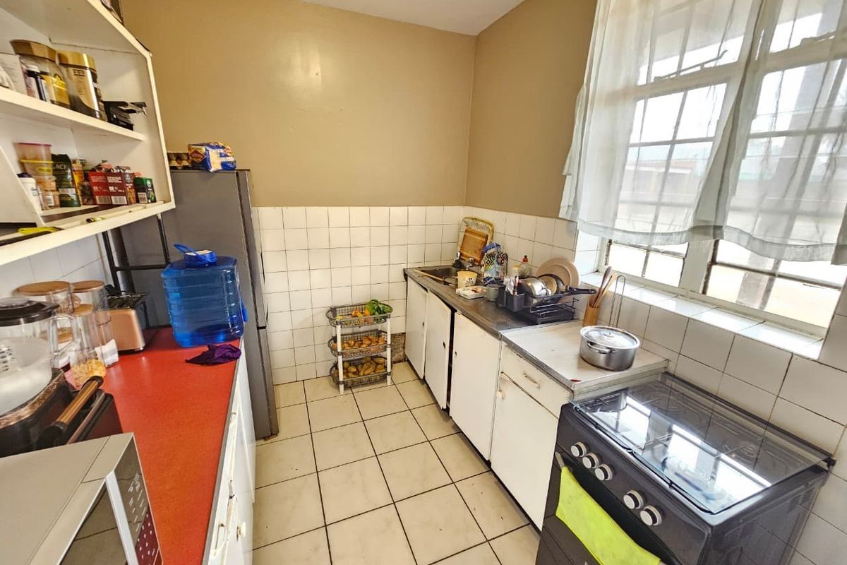 A functional kitchen featuring tiled flooring, a tiled backsplash, built-in cabinetry, and a freestanding stove, offering potential for modernization and cosmetic updates.