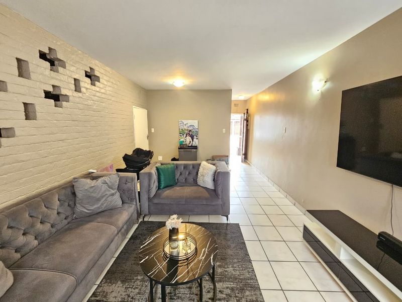 A spacious living room featuring ceramic floor tiles and a unique decorative brick feature wall, offering a neutral canvas for modern interior design updates.