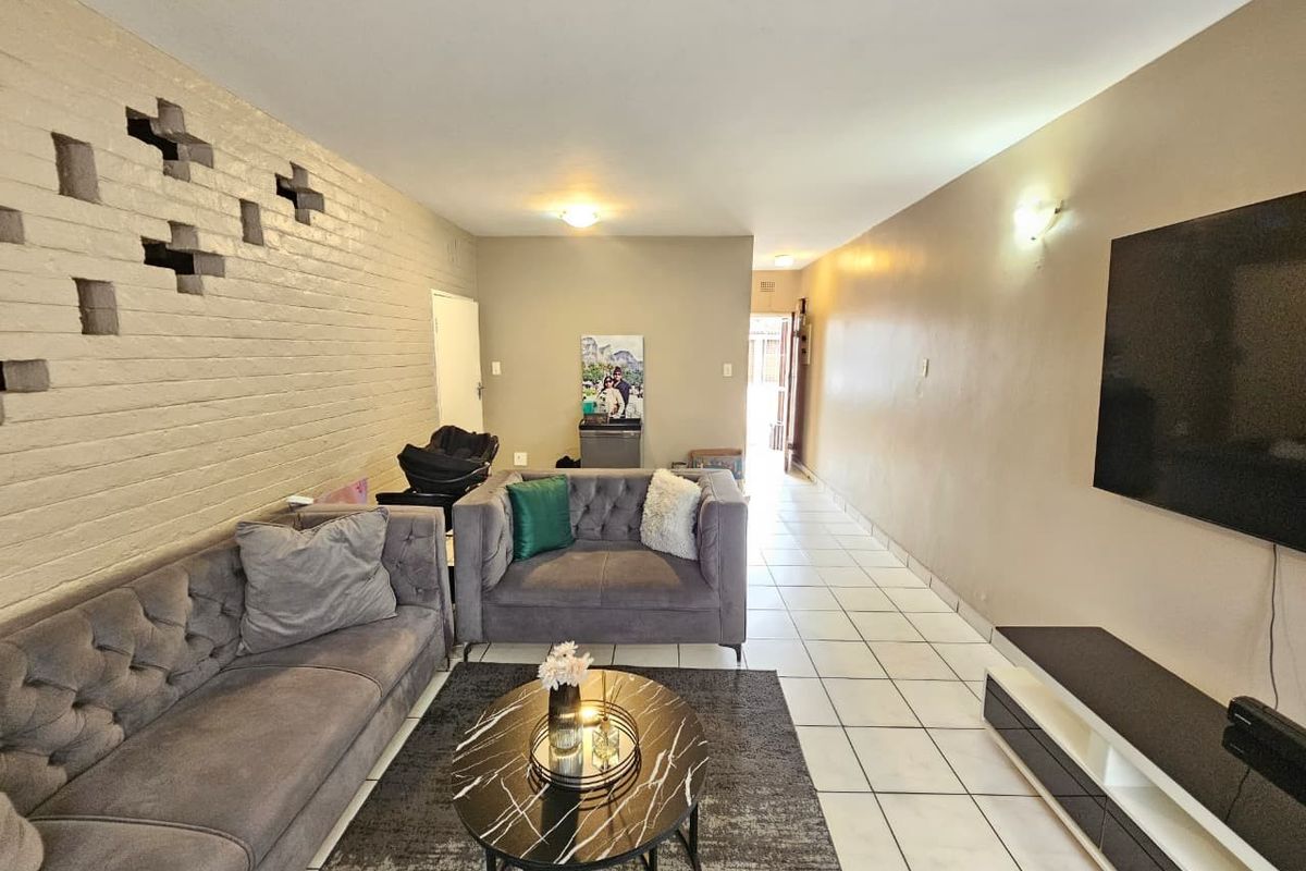 A spacious living room featuring ceramic floor tiles and a unique decorative brick feature wall, offering a neutral canvas for modern interior design updates.